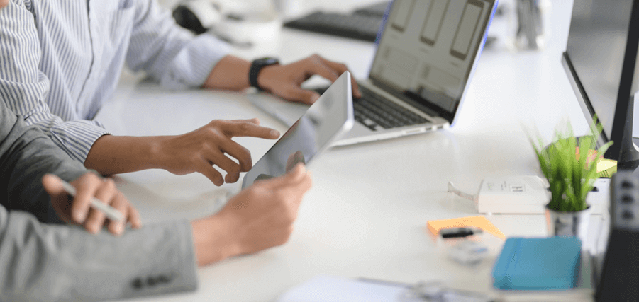 Two people sat at a desk with a laptop looking at a phone